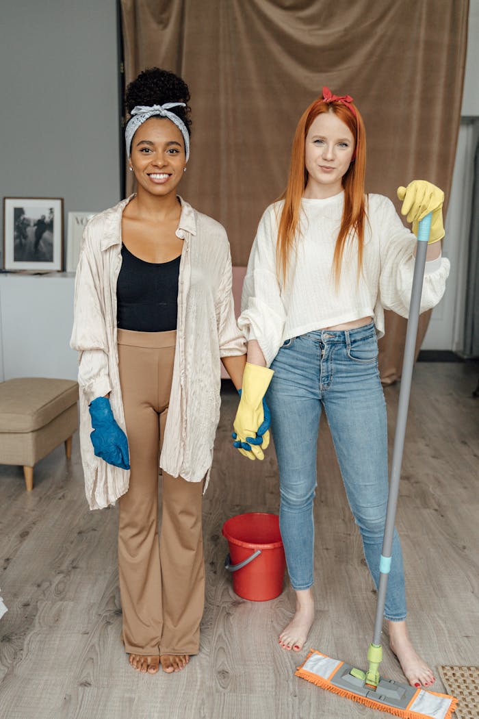 hero-img Two women smiling and holding hands while cleaning indoors, symbolizing teamwork.